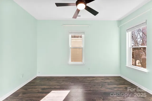 an empty room with wooden floor chandelier fan and windows