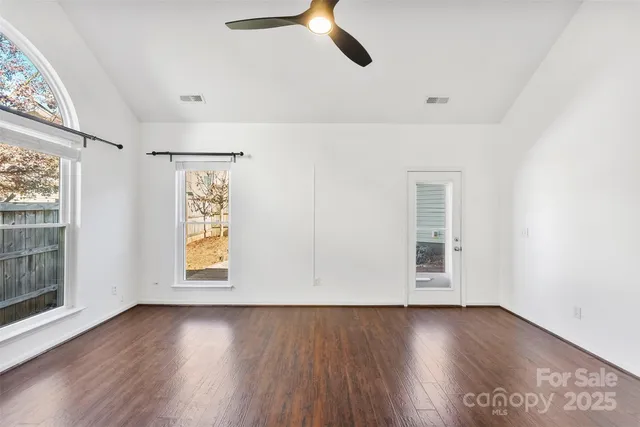 an empty room with wooden floor chandelier fan and windows