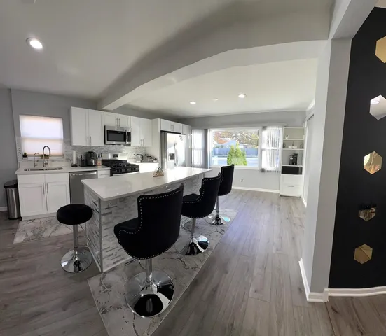 a kitchen with stainless steel appliances kitchen island hardwood floor sink stove dining table and chairs