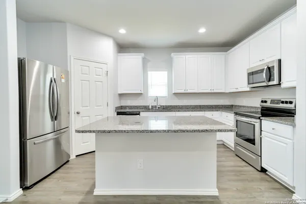 a kitchen with stainless steel appliances granite countertop a refrigerator a stove a sink and white cabinets