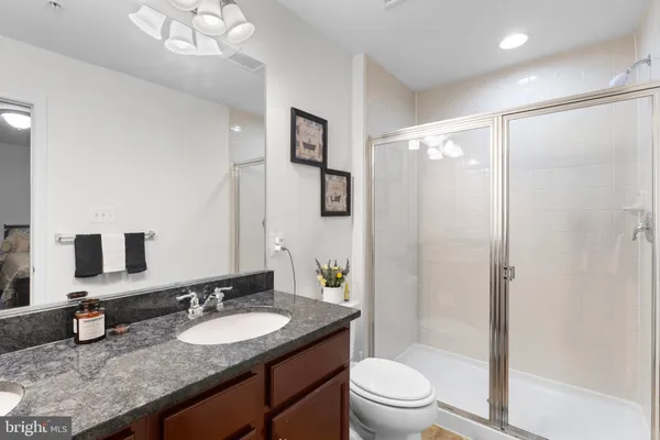 a bathroom with a granite countertop sink a toilet a mirror a vanity and shower