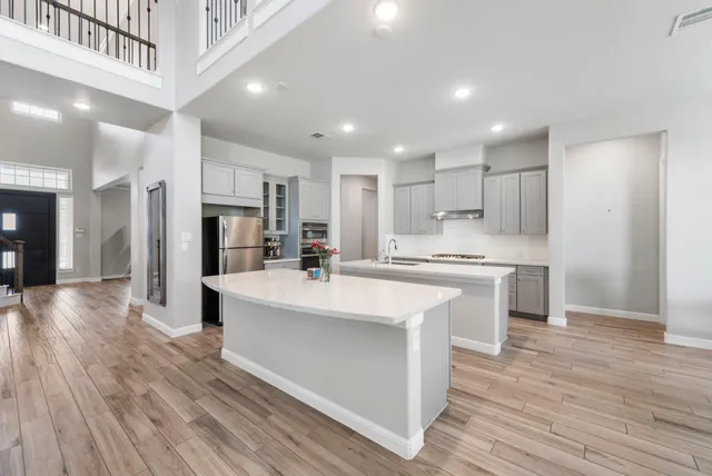 a large white kitchen with kitchen island a sink a stove a refrigerator and white cabinets with wooden floor