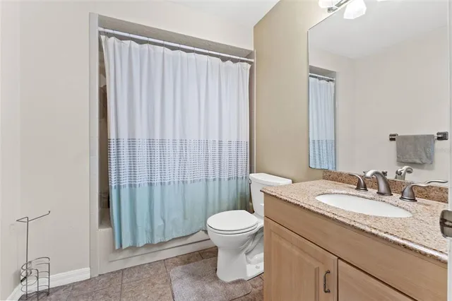 a bathroom with a granite countertop sink a toilet a mirror and shower curtain