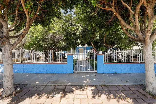 a view of a brick house with large trees and wooden fence