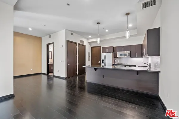 a large white kitchen with a large counter top stainless steel appliances and wooden floor