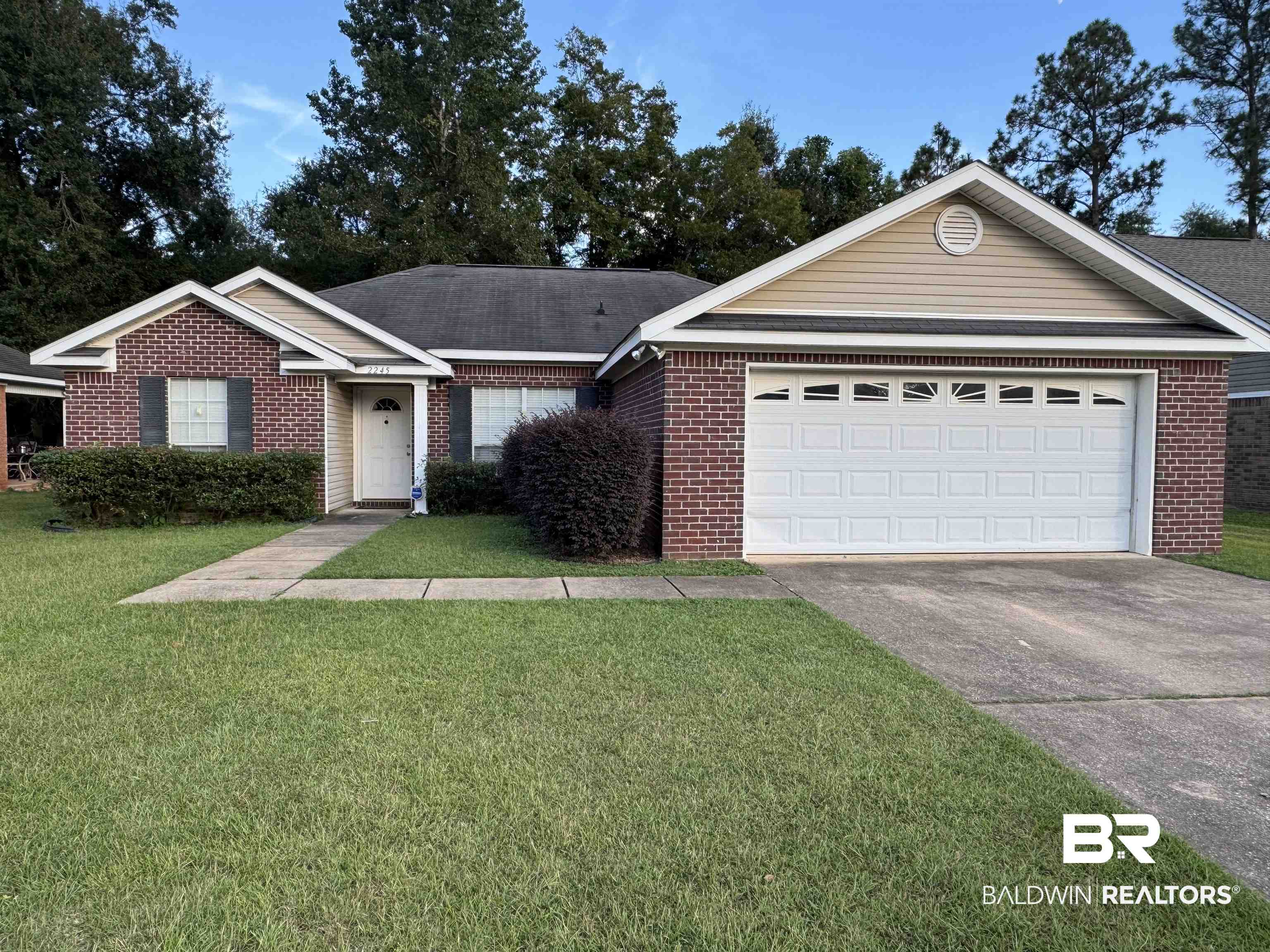 Ranch-style home with concrete driveway, a front lawn, brick siding, and roof with shingles