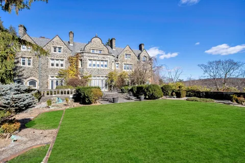 a view of a big yard in front of a brick house with large windows