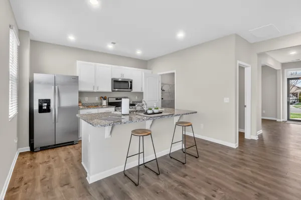 a kitchen with stainless steel appliances granite countertop a stove a sink a microwave a refrigerator and white cabinets with wooden floor