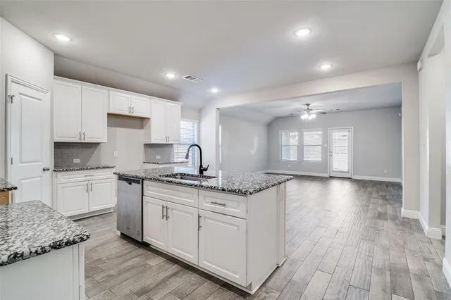 a kitchen with stainless steel appliances granite countertop a stove a sink and white cabinets with wooden floor