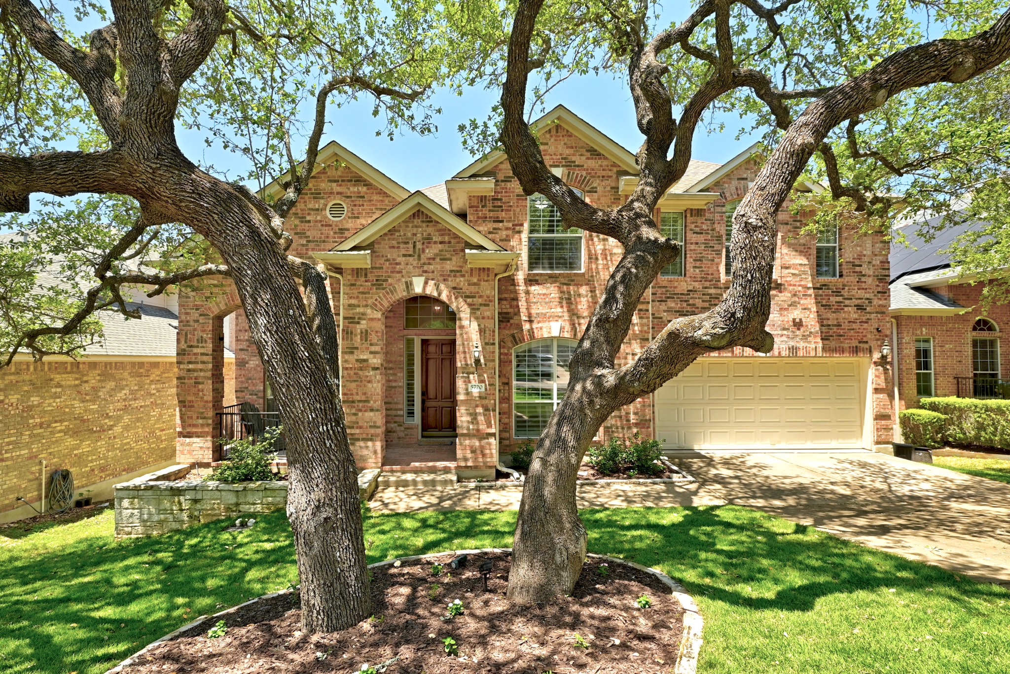 5720 Sunset Ridge Austin, TX 78735 - Photo 1 of 1 Brick facade residence featuring a three-car tandem garage, arched entryways, and a covered front porch with large trees