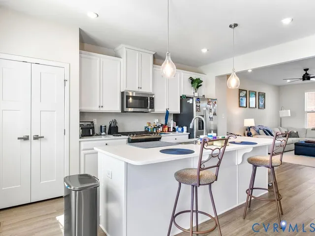 a kitchen with stainless steel appliances kitchen island granite countertop a refrigerator a stove a sink a dining table and chairs with wooden floor