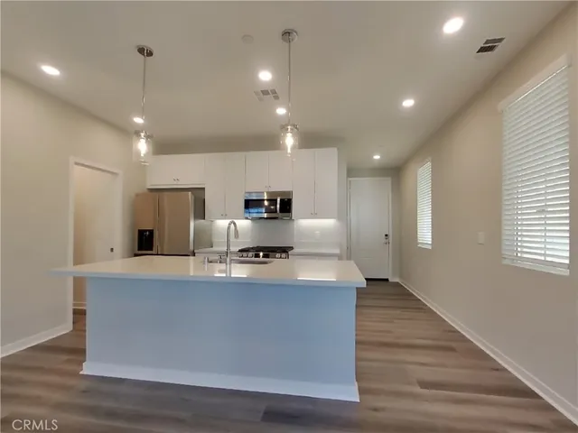 a large kitchen with stainless steel appliances a large counter top and wooden floors