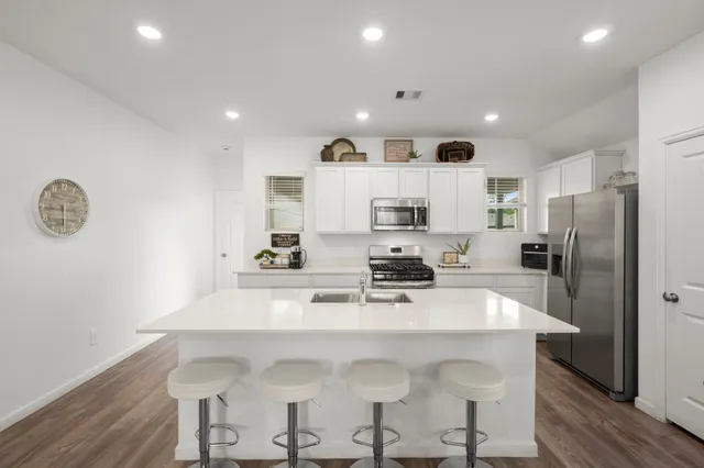 a kitchen with stainless steel appliances a sink a stove a refrigerator cabinets and a dining table