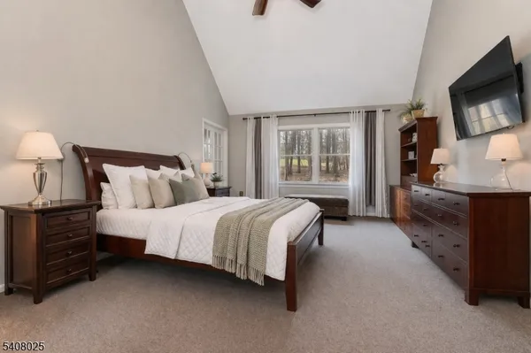a spacious bedroom with a bed and a flat tv screen on dresser