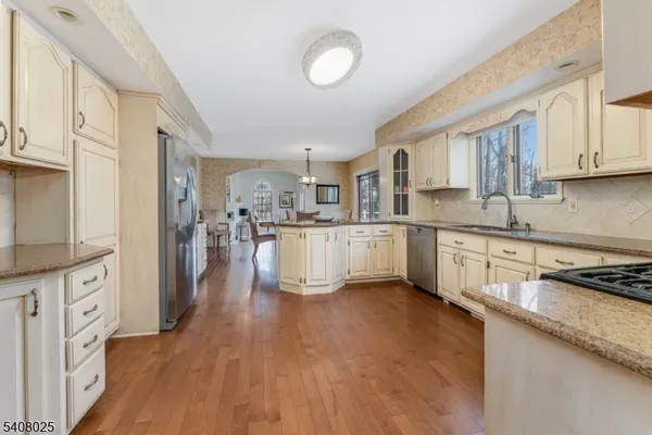 a kitchen with stainless steel appliances granite countertop a stove top oven a sink a refrigerator white cabinets and wooden floor