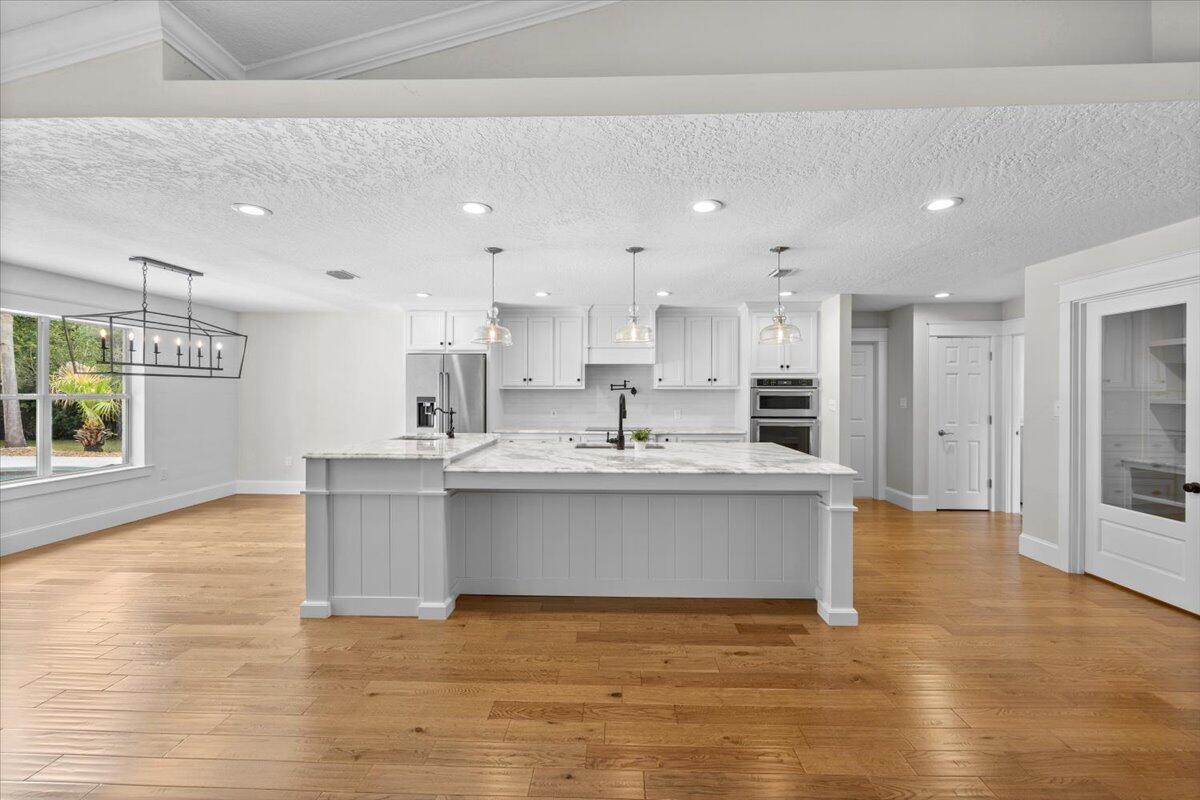 7584 Woodmont Road Navarre, FL 32566 - Photo 14 of 62 a large white kitchen with kitchen island a sink a stove a refrigerator and a dining table with wooden floor