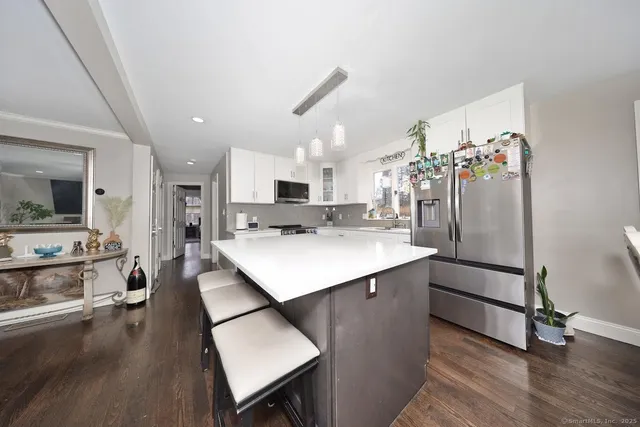 a kitchen with stainless steel appliances kitchen island granite countertop a refrigerator a stove a sink dishwasher and white cabinets with wooden floor