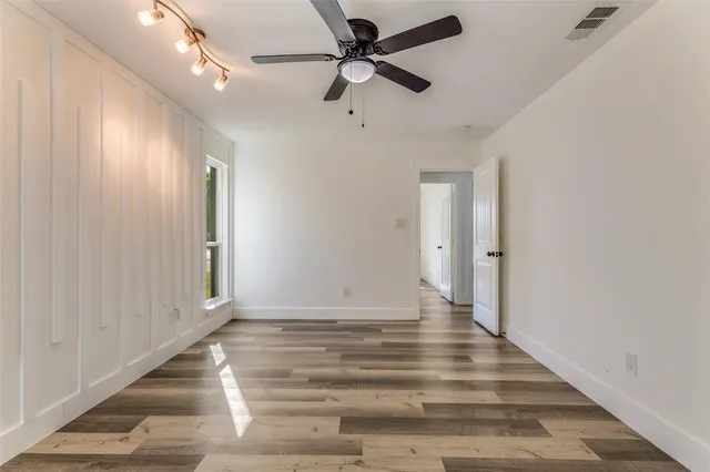 an empty room with wooden floor chandelier fan and windows