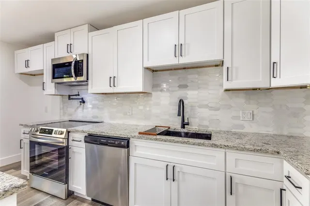 a kitchen with stainless steel appliances granite countertop a sink a stove a refrigerator and white cabinets