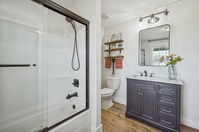 a bathroom with a granite countertop sink a toilet a mirror and shower