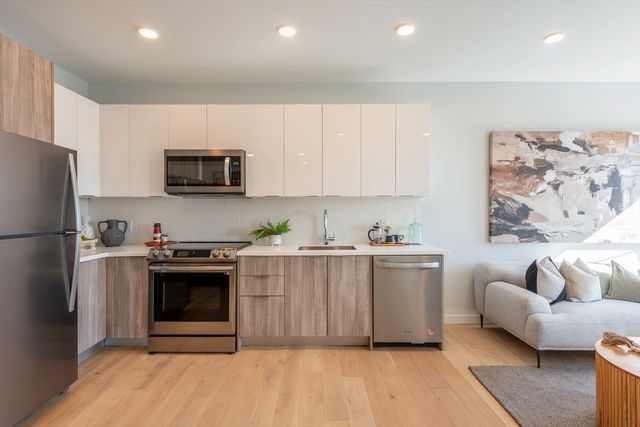 a kitchen with stainless steel appliances a stove a microwave a sink a refrigerator white cabinets and wooden floor