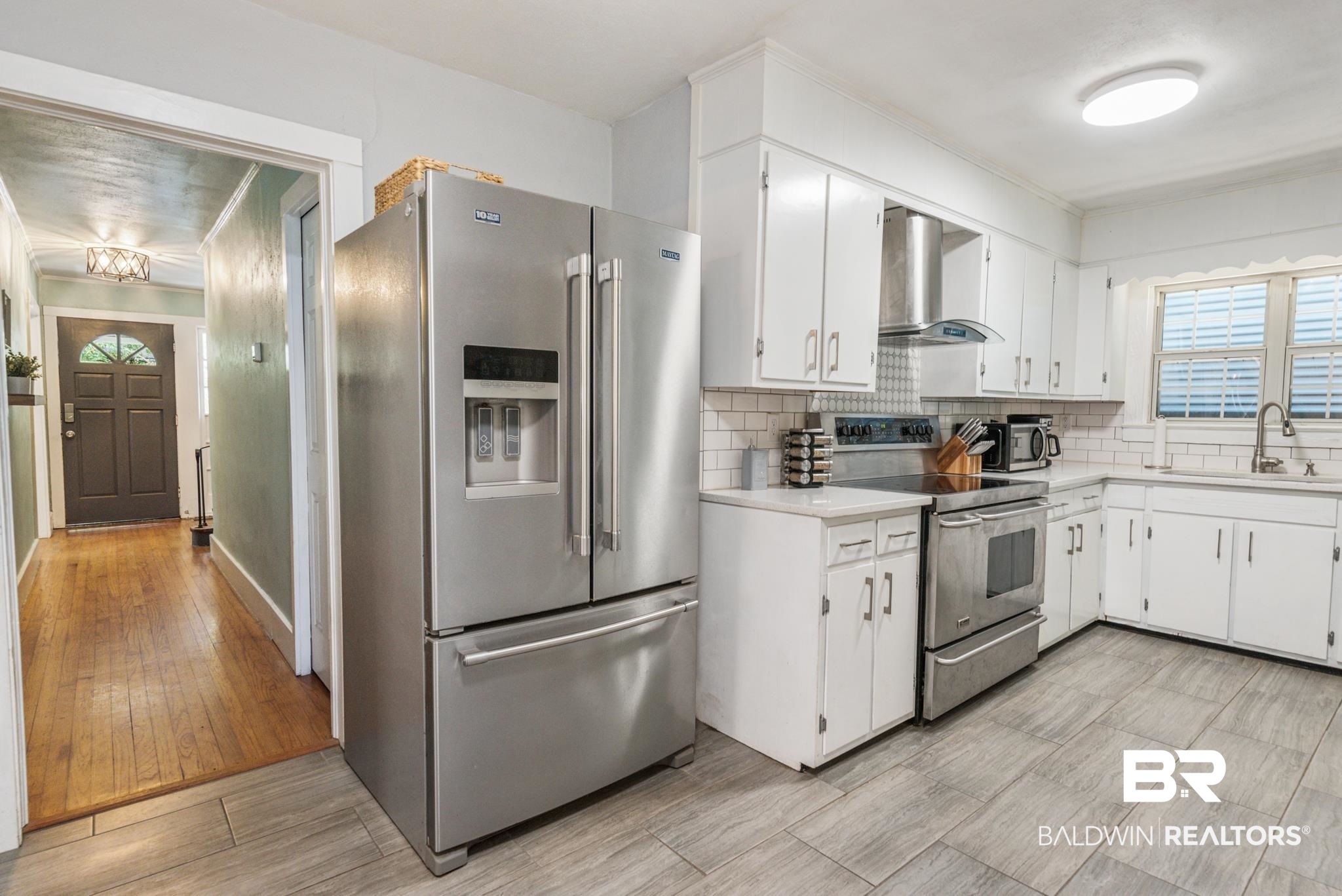 114 Crenshaw Street Mobile, AL 36606 - Photo 18 of 49 Kitchen featuring white cabinets, light hardwood / wood-style floors, wall chimney exhaust hood, appliances with stainless steel finishes, and sink