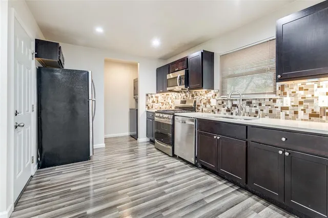 a kitchen with stainless steel appliances granite countertop a refrigerator a sink dishwasher and a large mirror with wooden cabinets