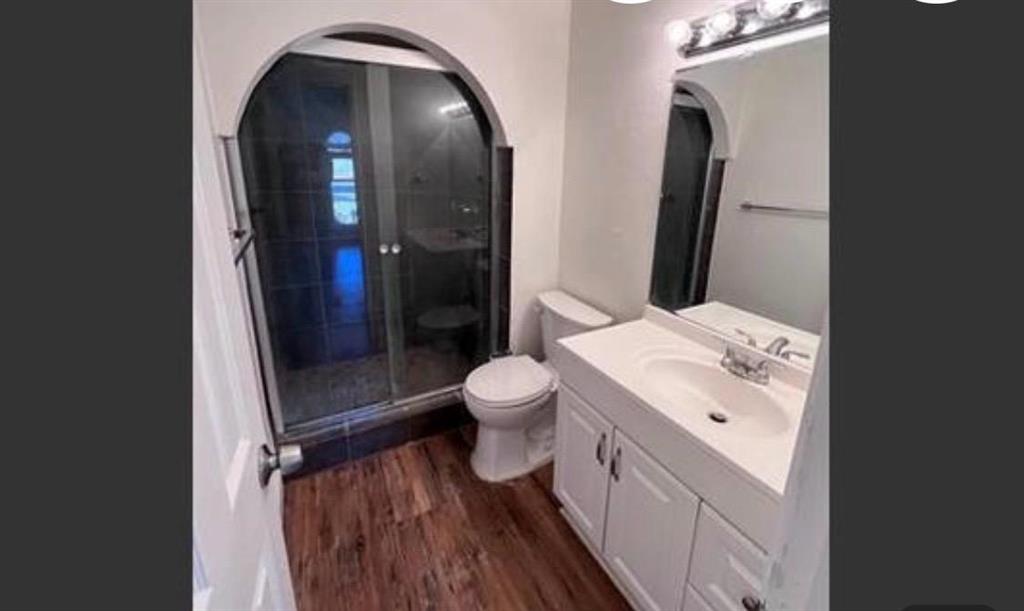 4422 Galaxie Road Garland, TX 75044 - Photo 9 of 11 Bathroom featuring a glass-enclosed shower with an arched opening, a white vanity with integrated sink, wood-finish flooring, a wall-mounted mirror, and a chrome light fixture