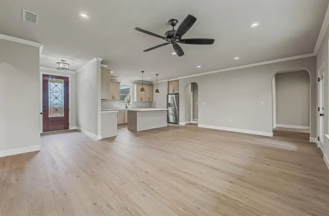 a view of an empty room with wooden floor and a ceiling fan