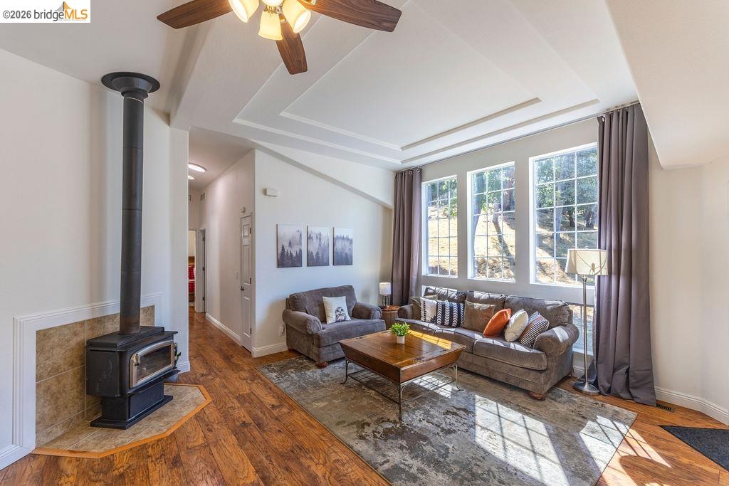20828 Ferretti Road Groveland, CA 95321 - Photo 10 of 60 Living area with ceiling fan, a wood stove, a tray ceiling, and wood finished floors