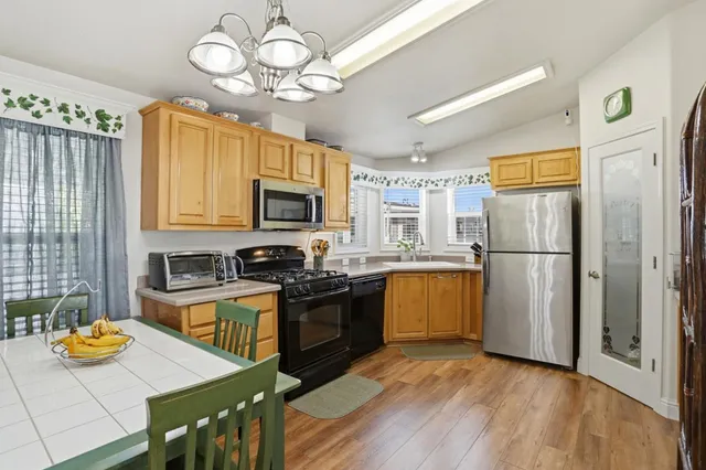a kitchen with stainless steel appliances granite countertop a refrigerator a stove top oven a sink dishwasher and wooden cabinets with wooden floor