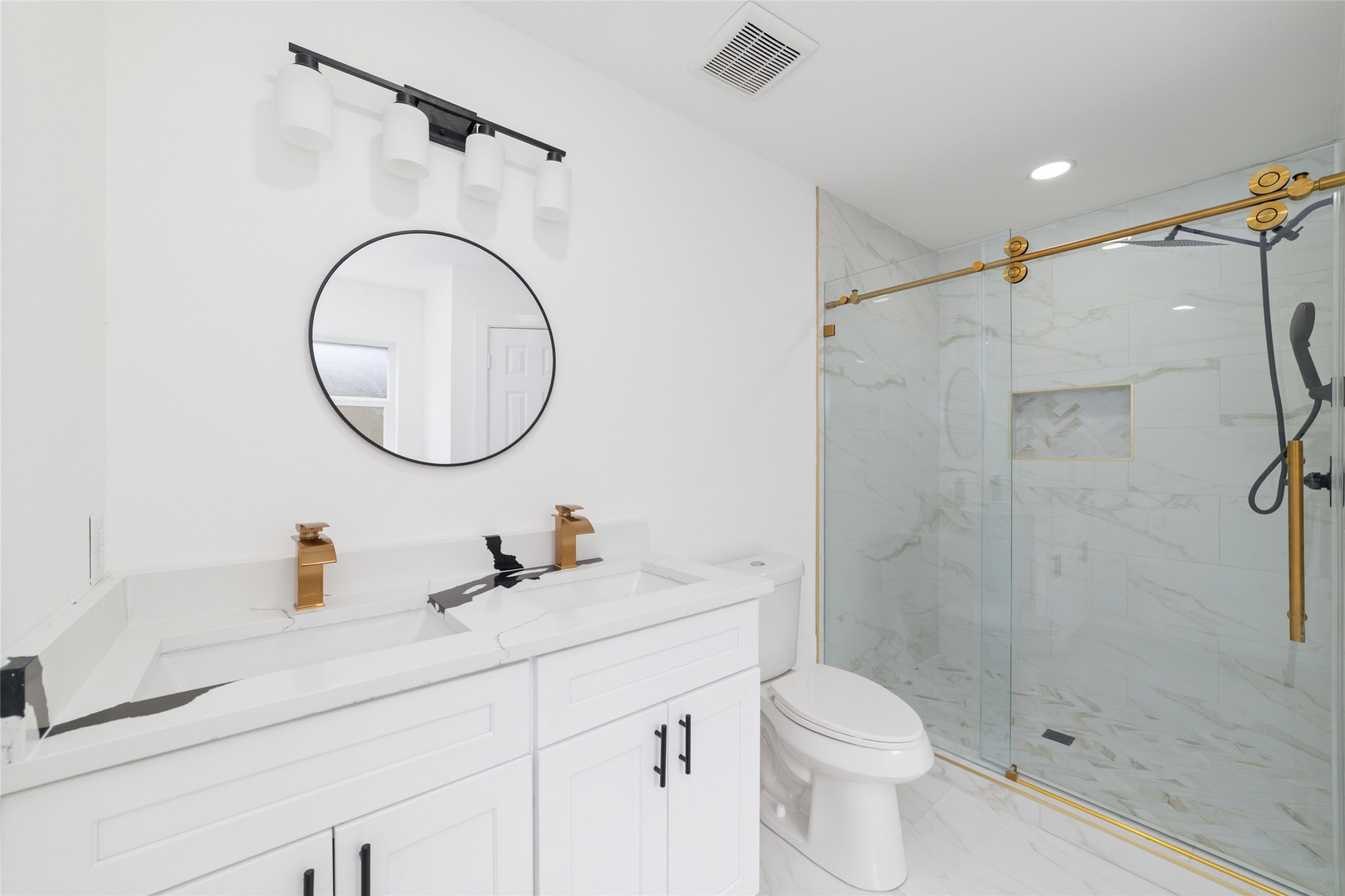 5709 Langley Road Houston, TX 77016 - Photo 16 of 27 This bathroom features a modern design with a sleek double vanity, gold fixtures, a round mirror, and a spacious glass-enclosed shower with marble-style tiles.