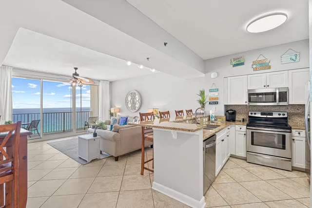 a living room with stainless steel appliances furniture a rug and a kitchen view