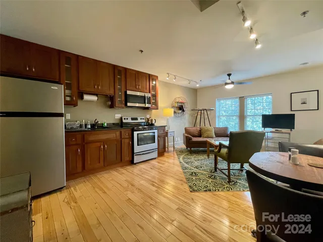 a kitchen with stainless steel appliances kitchen island granite countertop a refrigerator a stove a sink dishwasher a dining table and chairs with wooden floor