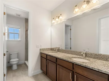 a bathroom with a granite countertop double vanity sink a toilet and a mirror