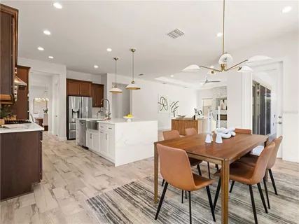 a dining room kitchen with stainless steel appliances kitchen island granite countertop a table chairs and a refrigerator