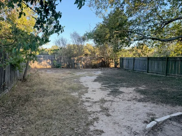 a view of a yard with large trees and wooden fence