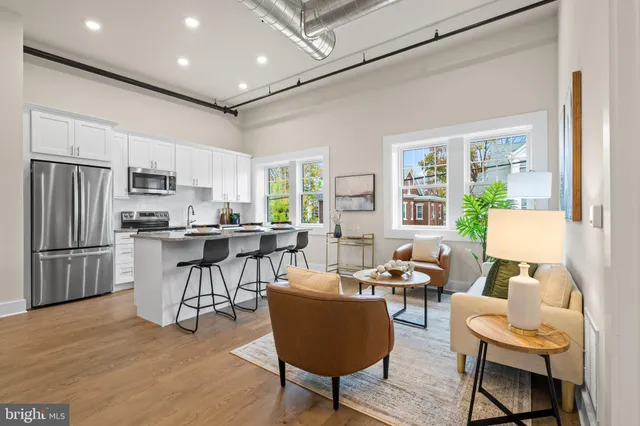 a living room with stainless steel appliances kitchen island granite countertop furniture a refrigerator a kitchen island a stove and a dining table with wooden floor