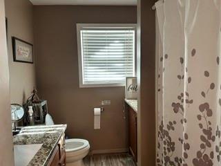 2924 Windsor Avenue Waco, TX 76708 - Photo 21 of 25 Wood-finish flooring with a white toilet, a window with horizontal blinds, and a vanity featuring a patterned countertop and wood cabinetry