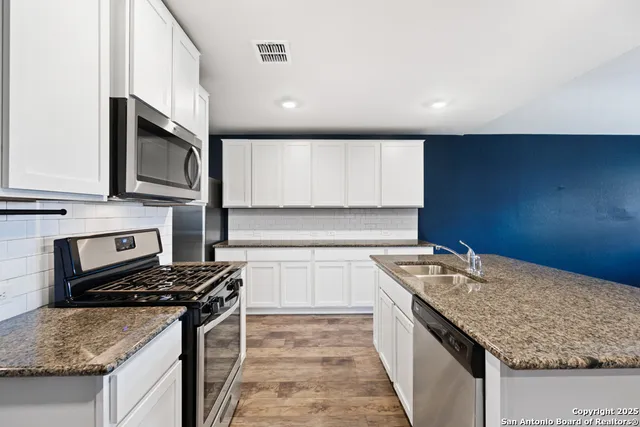 a kitchen with stainless steel appliances granite countertop a stove top oven a sink a refrigerator white cabinets and wooden floor