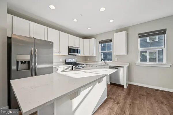 a large kitchen with kitchen island a sink a stove a refrigerator and white cabinets with wooden floor