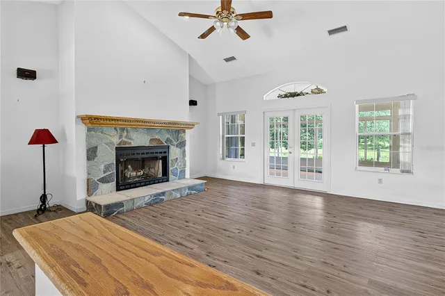 an empty room with windows a fireplace a ceiling fan and wooden floor