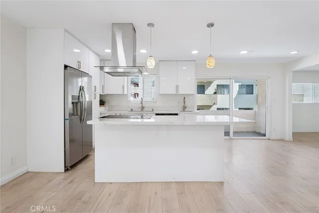 a large white kitchen with kitchen island a large counter top a sink stainless steel appliances and cabinets