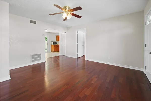 an empty room with wooden floor chandelier fan and windows