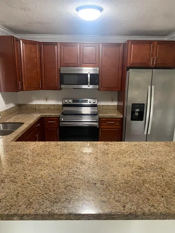 a kitchen with kitchen island granite countertop wooden cabinets a stove a oven and a refrigerator with wooden floor