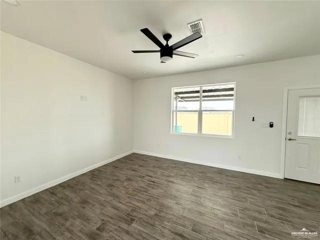 an empty room with wooden floor ceiling fan and windows