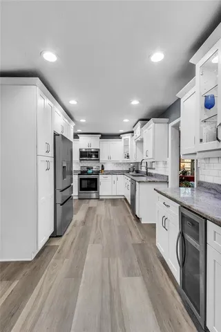 a kitchen with stainless steel appliances granite countertop a refrigerator oven a sink dishwasher and white cabinets with wooden floor