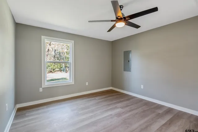 a view of an empty room with wooden floor and a ceiling fan