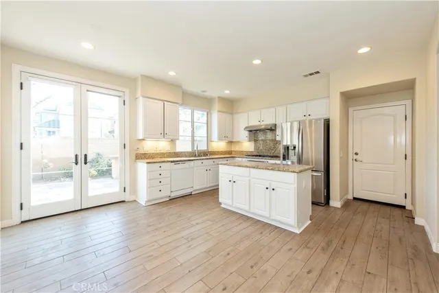 a large kitchen with a lot of white cabinets wooden floor and stainless steel appliances