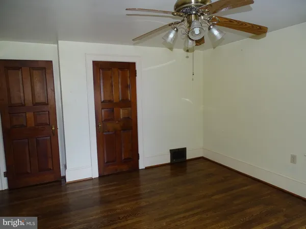 a view of an empty room with wooden floor and fan